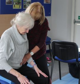 older woman sitting in a chair with tutor practising Alexander Technique
