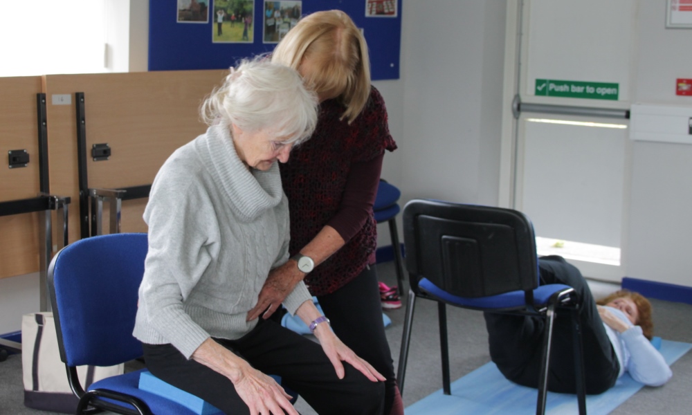 older woman sitting in a chair with tutor practising Alexander Technique