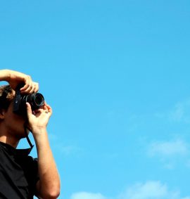 Person holding Black digital camera with blue sky behind