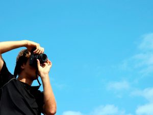 Person holding Black digital camera with blue sky behind