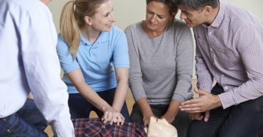 Woman Demonstrating CPR On Training Dummy In First Aid Class