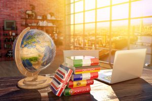 A globe, a pile of language books and a laptop on a desk