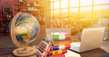 A globe, a pile of language books and a laptop on a desk