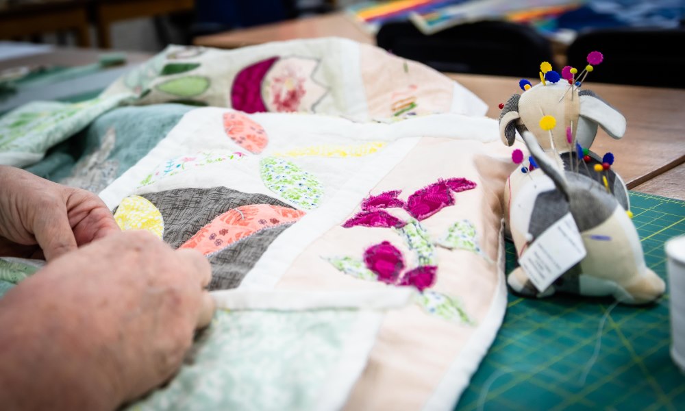 Hands working on a patchwork quilt with pin cushion