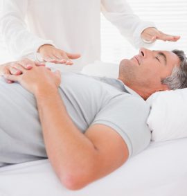 man lying on bed with woman performing reiki