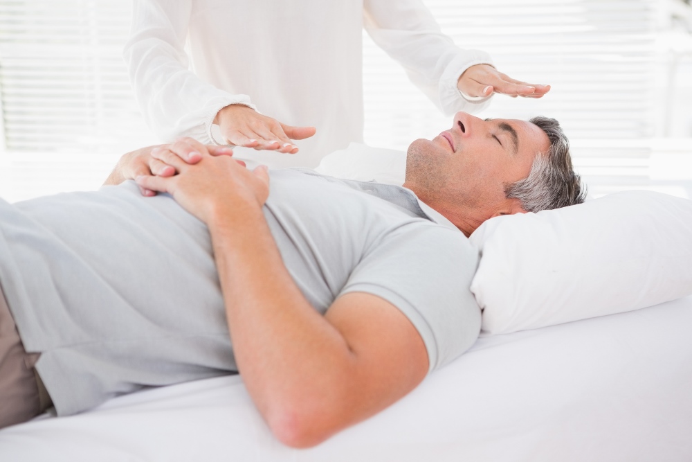 Man lying on bed with someone practising reiki