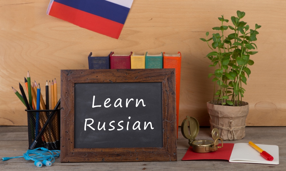 Blackboard with Learn Russian written with pencils and books behind