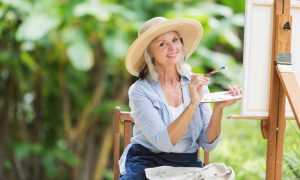 Woman in a hat painting on an easel outside