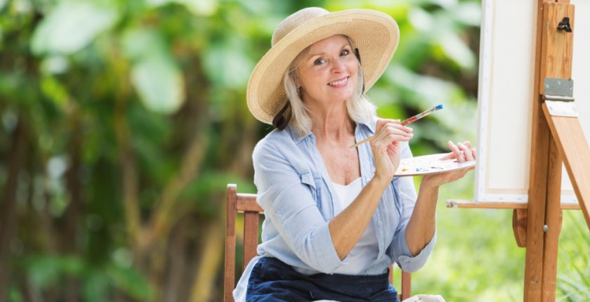 Woman in a hat painting on an easel outside