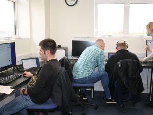 three people working on computers in a classroom with a tutor
