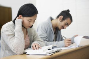 Image of two students sitting in a lecture hall and studying for exams