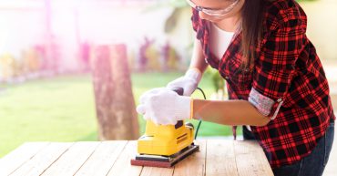 Woman Carpenter working with wood electrical sanding machine